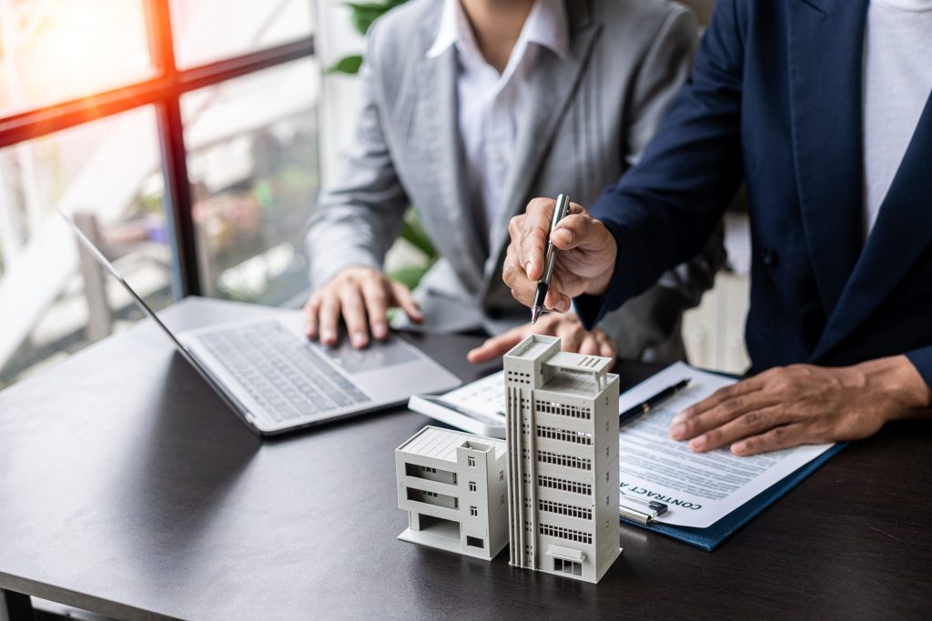 Hands of two investors working at a desk with laptop, notes, and a commercial building model