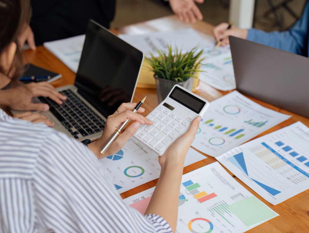 Desk view with spreadsheets, calculators, and laptops showing investors working with CRM data and tools